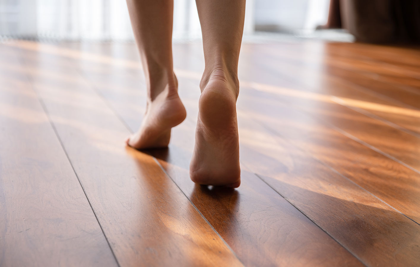 Nackte Füße laufen über einen Parkettboden